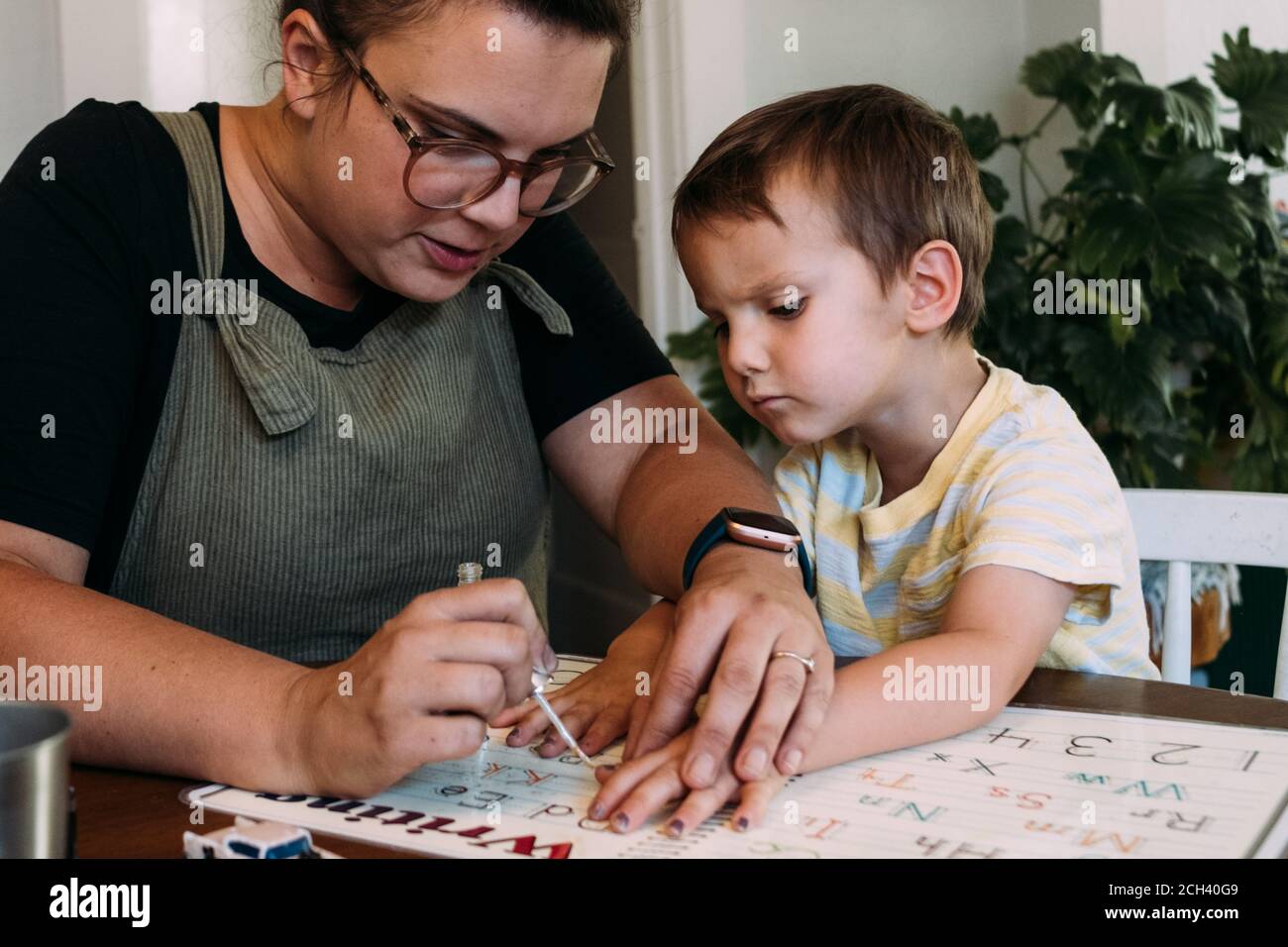 Maman peignant les ongles des doigts de son jeune fils à la table de salle à manger Banque D'Images