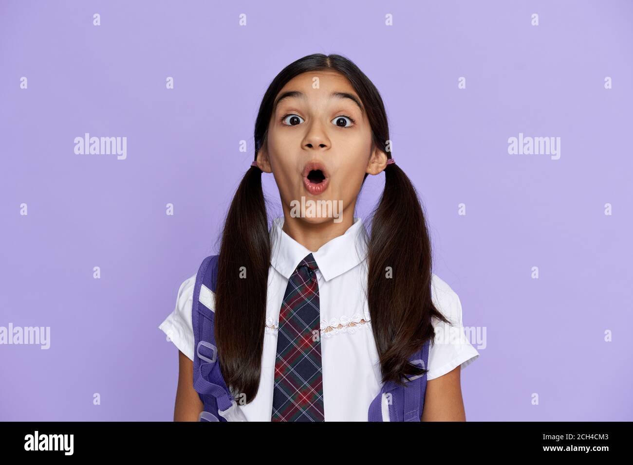 Drôle étonnant école indienne fille regardant l'appareil photo isolé sur fond violet. Banque D'Images