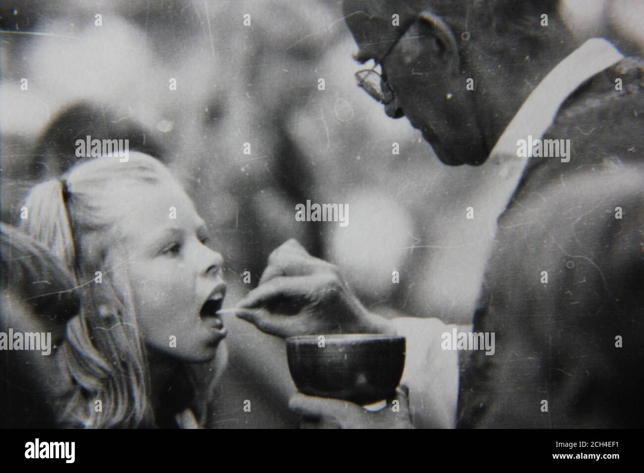 Belle photo vintage des années 70 en noir et blanc d'une fille recevant la communion sainte d'un prêtre à la messe du dimanche. Banque D'Images