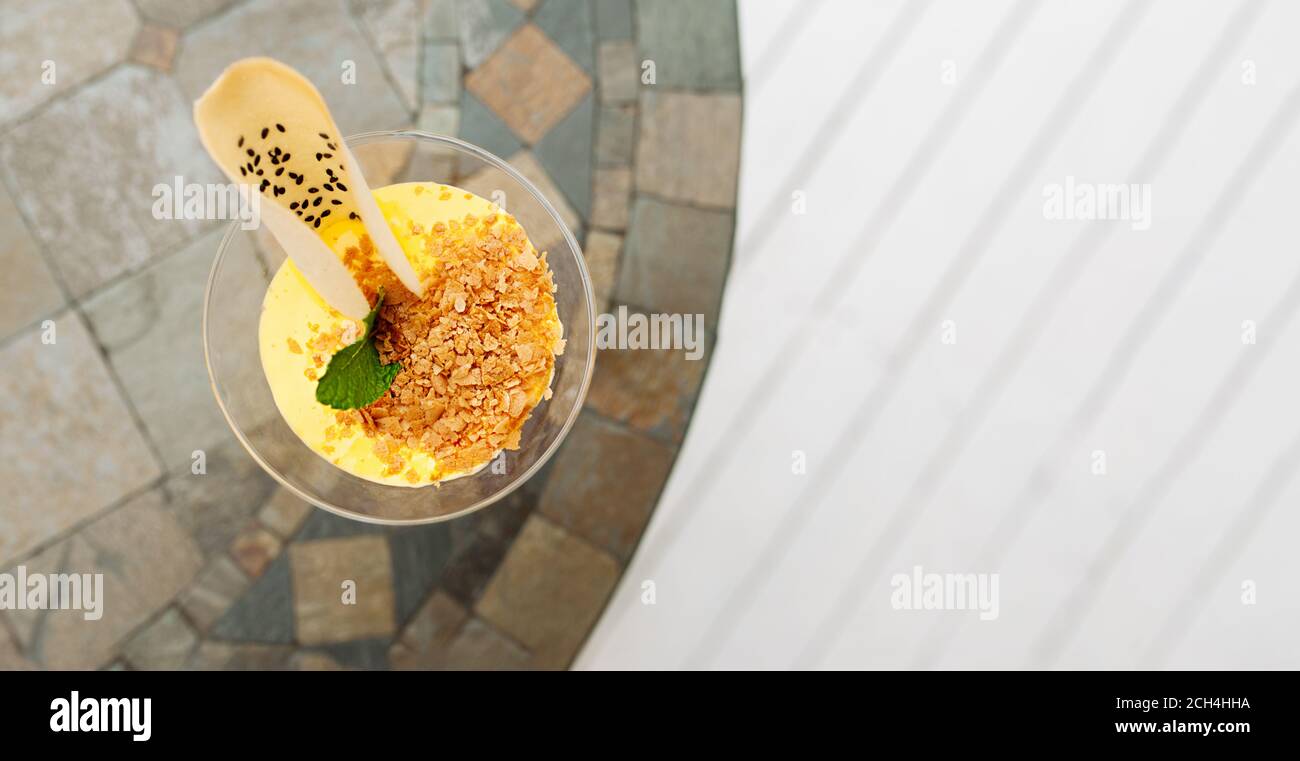 verre élégant avec dessert mousse jaune, biscuits et garniture sur table ronde, bannière grand format, mise au point sélective Banque D'Images