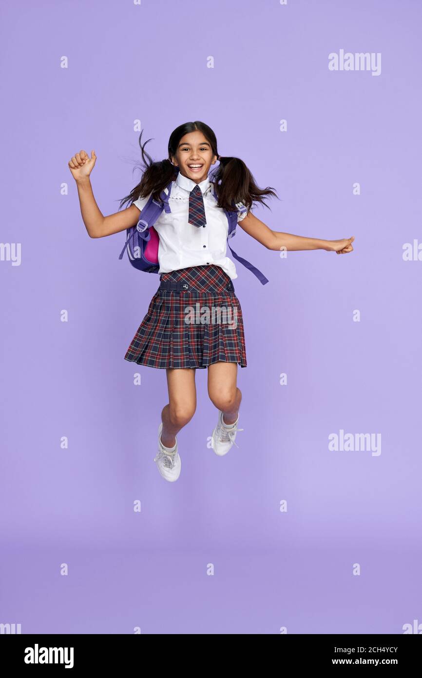 Excitée heureuse école indienne fille sautant isolé sur fond violet. Banque D'Images
