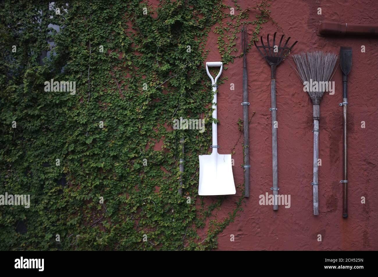 Les outils de jardinage accrochés au mur de ciment rouge. Banque D'Images