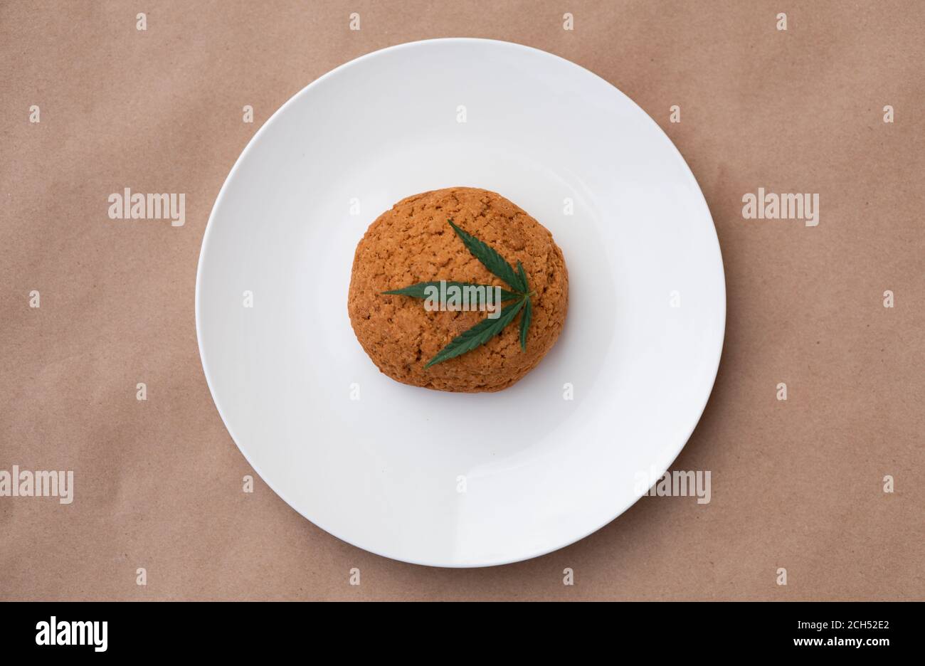 Feuille de cannabis avec biscuits sur une assiette blanche. Extraction de résine vivante de cannabis sur fond kraft. Banque D'Images