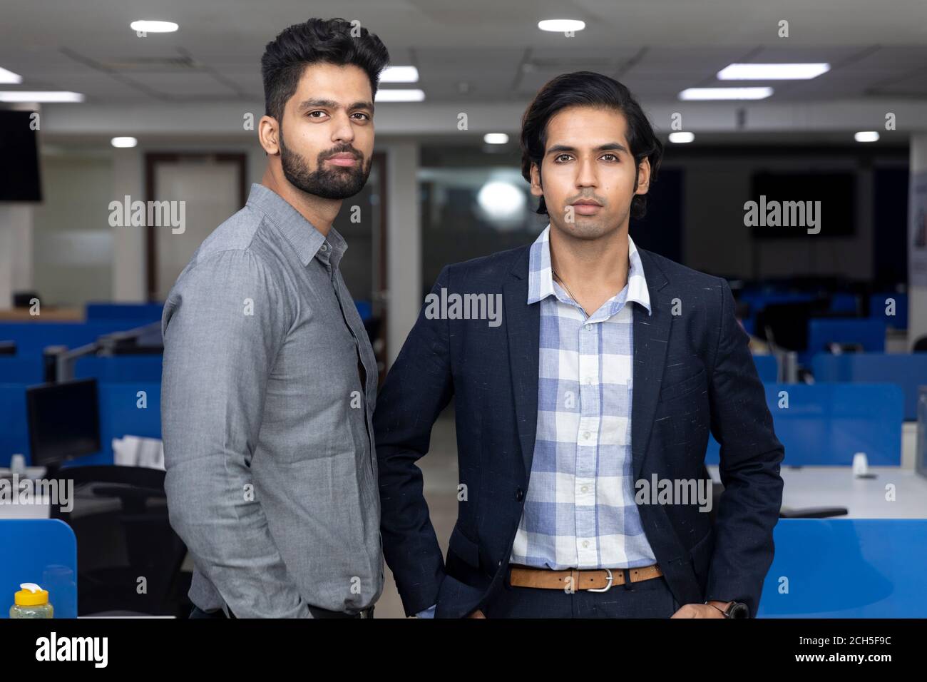 Portrait de deux jeunes hommes d'affaires indiens beaux debout contre le fond du bureau, l'environnement d'entreprise. Banque D'Images