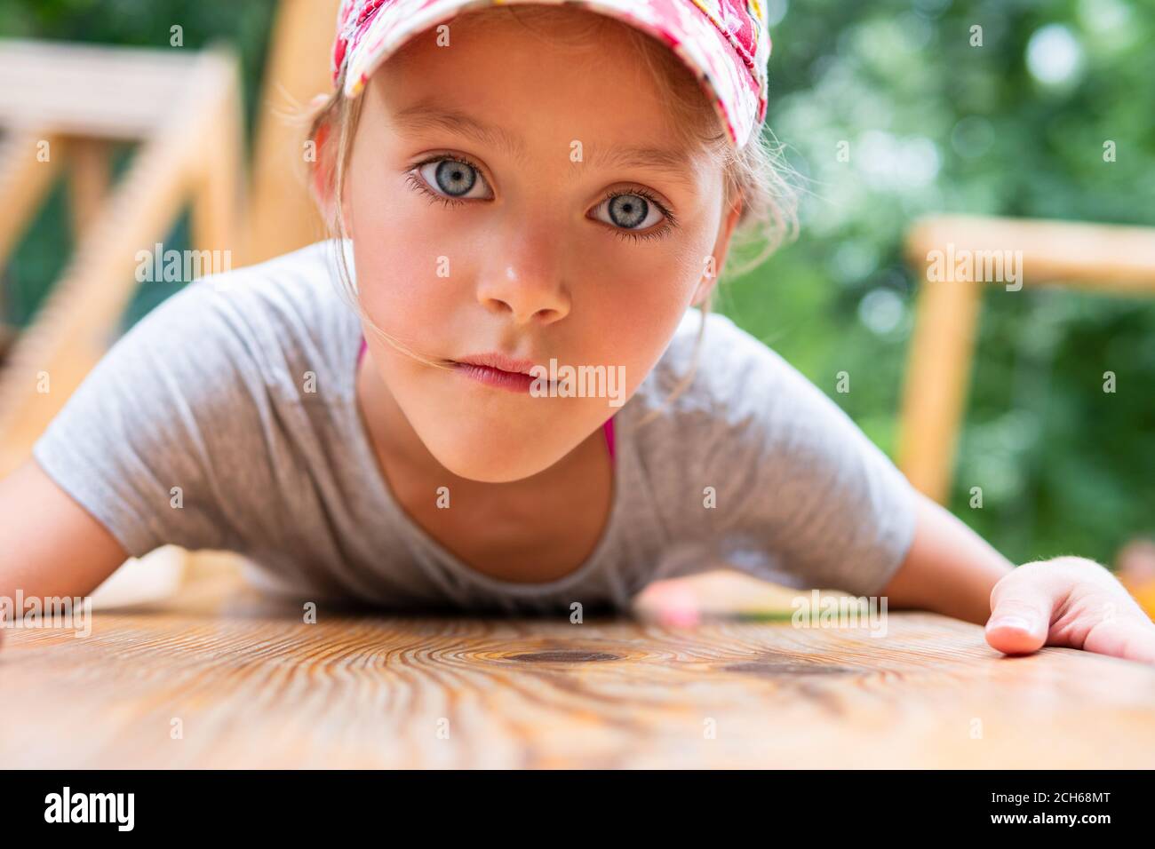 Portrait d'une petite fille dans un chapeau allongé sur son ventre sur une planche en bois dans le parc, gros plan. Enfant fille avec de grands yeux bleus. Banque D'Images