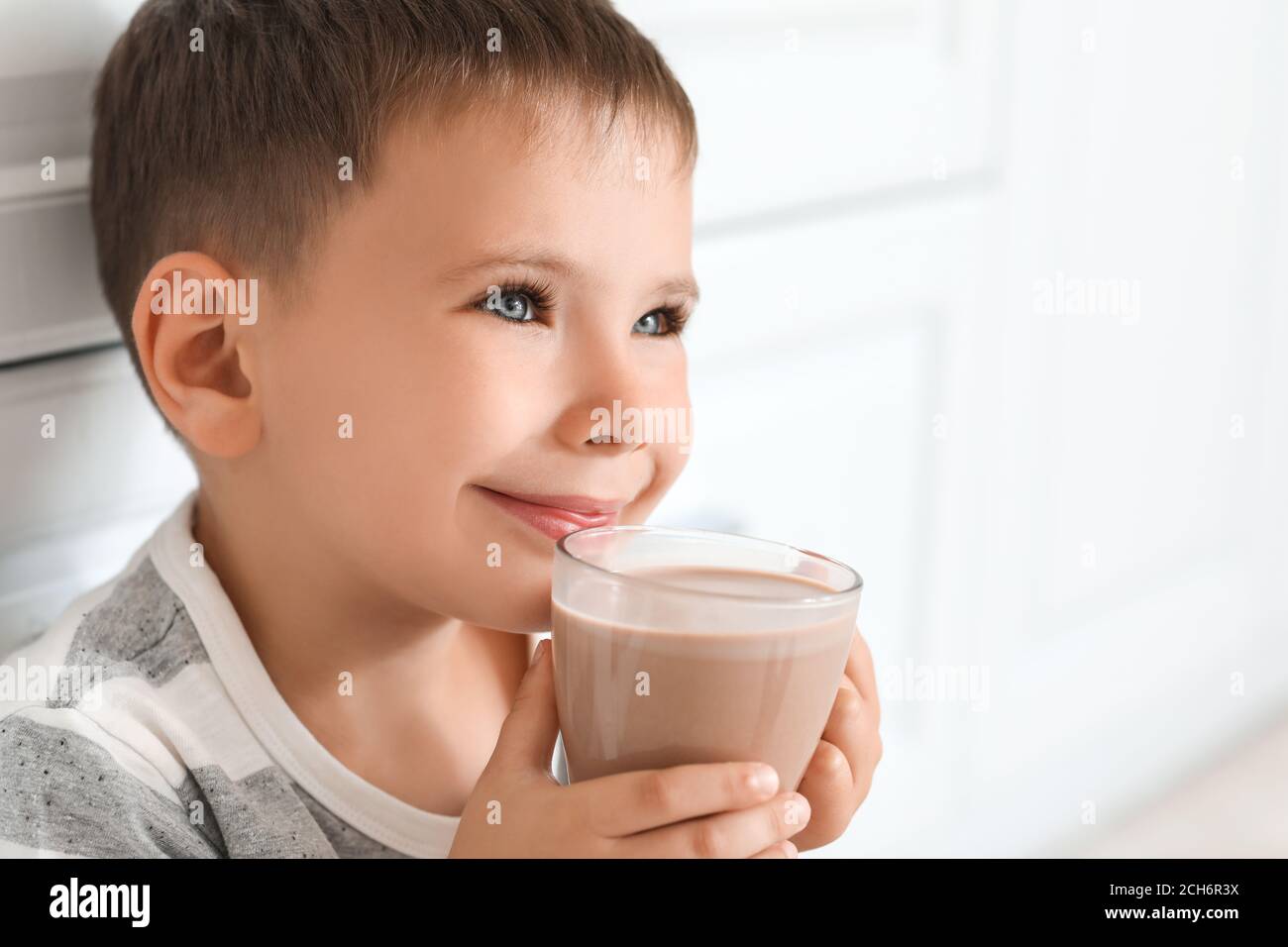 Un petit garçon boit du lait au chocolat savoureux à la maison Banque D'Images