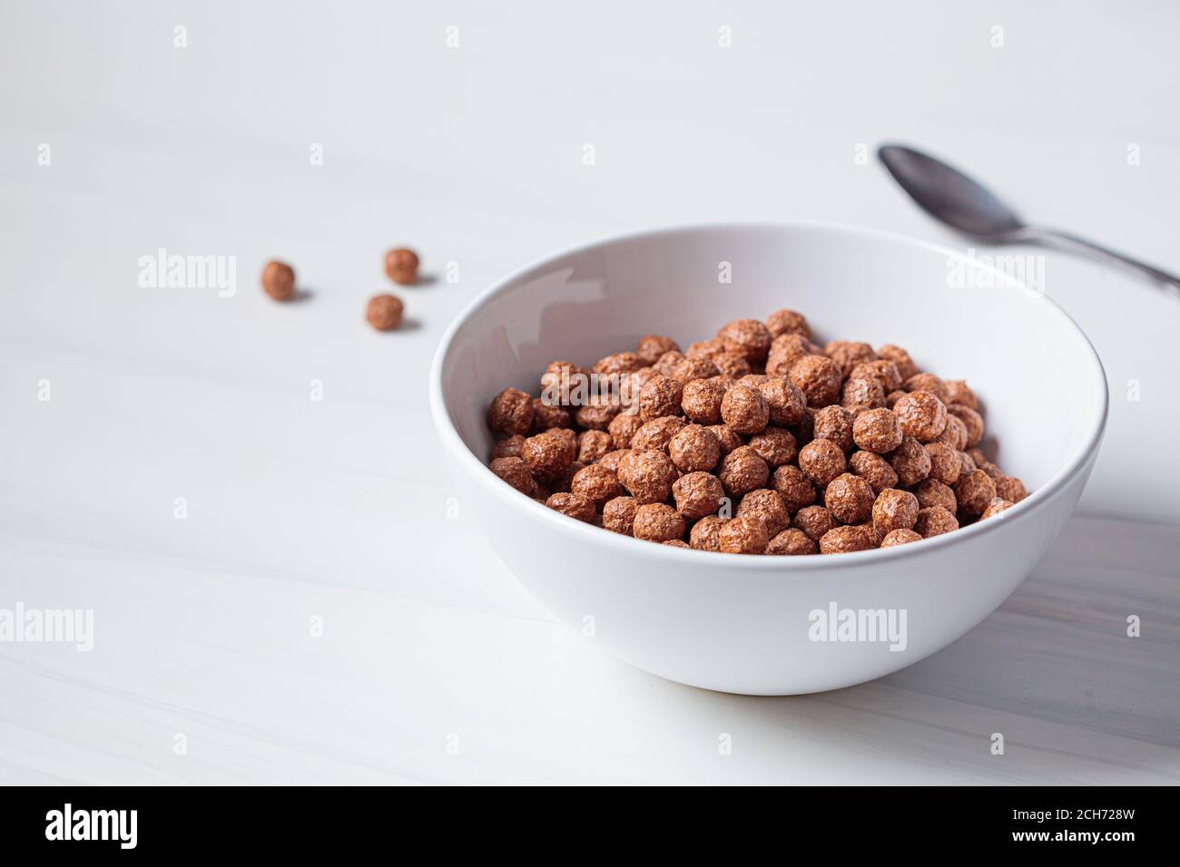 Boules de chocolat flocons de maïs dans un bol blanc, fond blanc. Concept de la nourriture pour le petit déjeuner. Banque D'Images