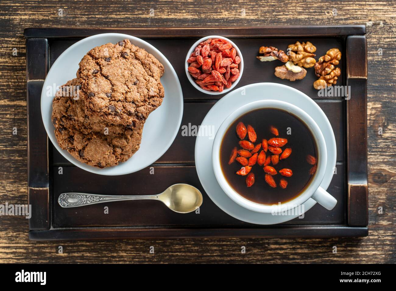 Tasse blanche de café goji frais du matin avec biscuits sur plateau en bois sur la table, vue du dessus, gros plan. Café chaud noir avec baies de goji rouges entières Banque D'Images