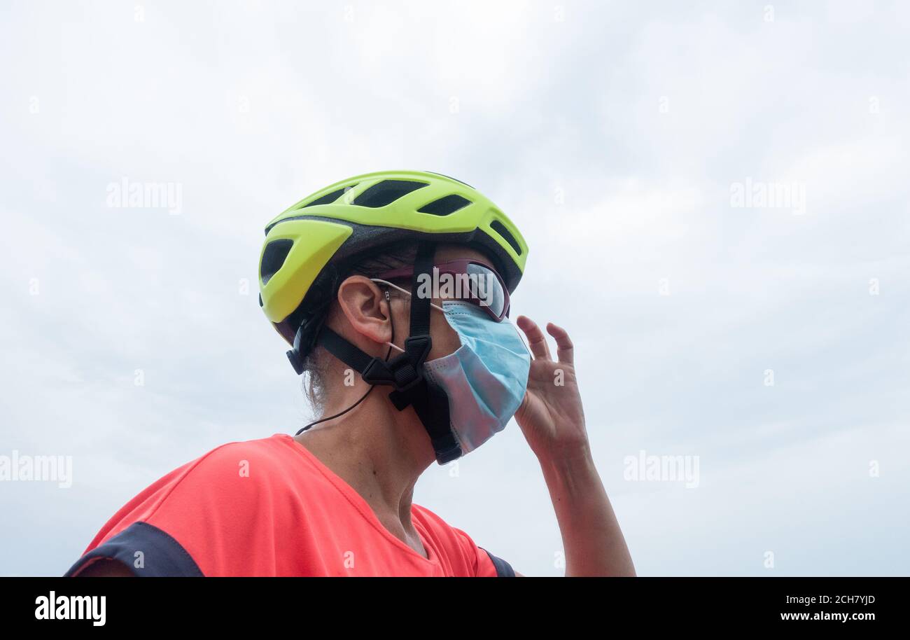 Cycliste adulte portant un casque de cyclisme, des lunettes de soleil et un masque facial, couvrant. Banque D'Images