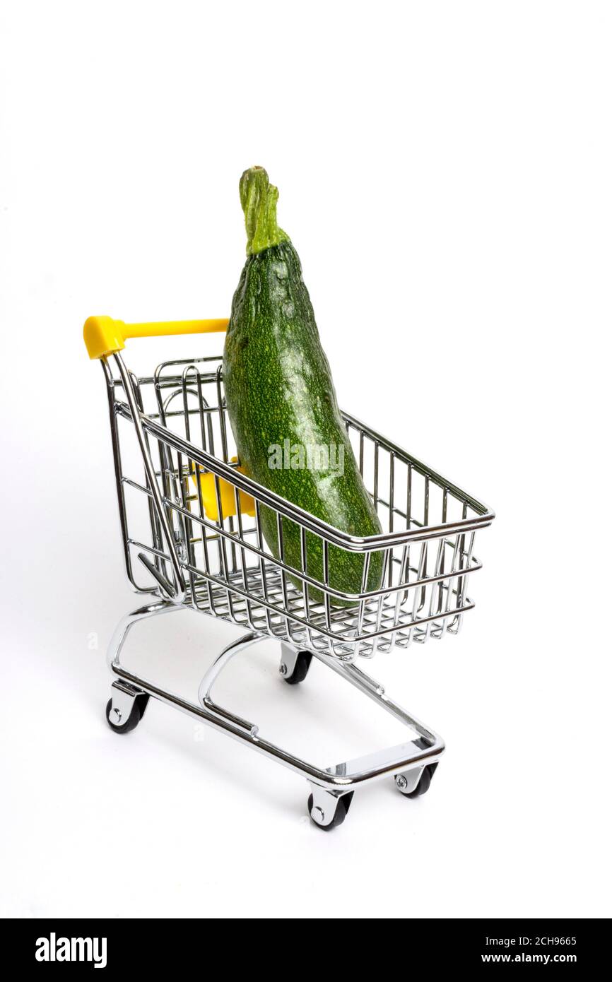 Chariot d'épicerie avec une grande courgette sur fond blanc, présentant des choix alimentaires sains et des achats de légumes Banque D'Images