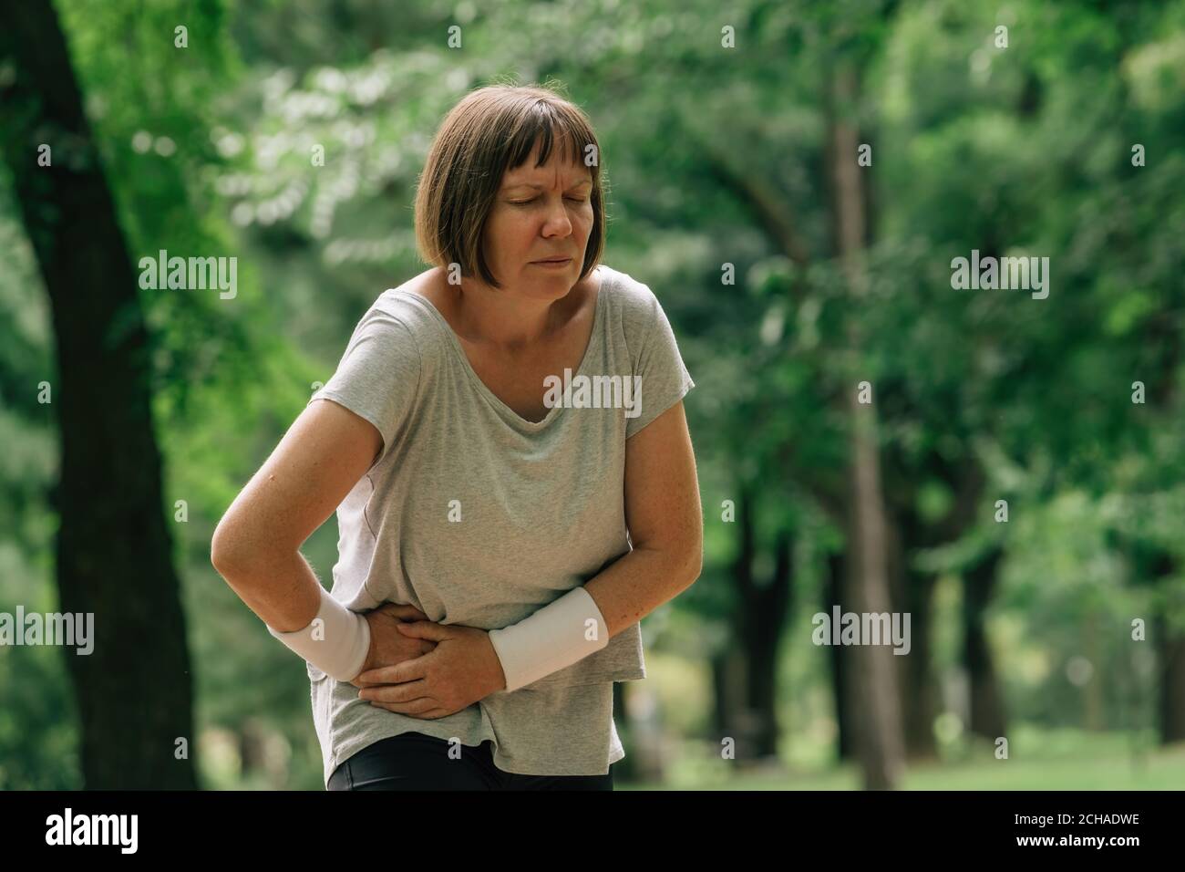 Jogging féminin avec grimace douloureux de visage après avoir ressenti la douleur dans abaisser l'abdomen pendant la course en position de stationnement Banque D'Images