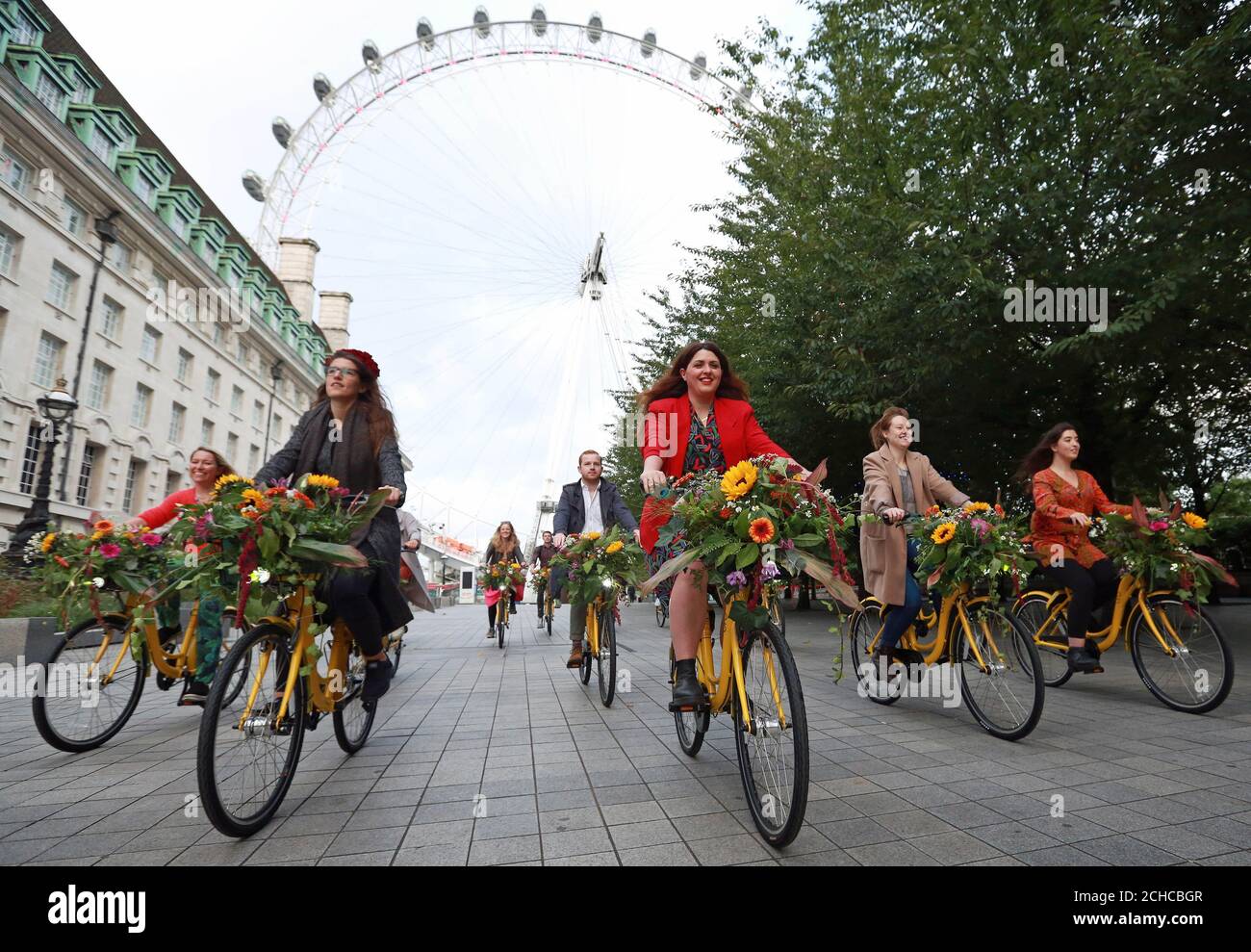 USAGE ÉDITORIAL SEULS les cyclistes utilisent des vélos Ofo jaunes au London Eye de Londres, avec des fleurs purifiantes de l'air dans leurs paniers, pour marquer la Journée mondiale sans voiture, qui a lieu le vendredi 22 septembre. Banque D'Images