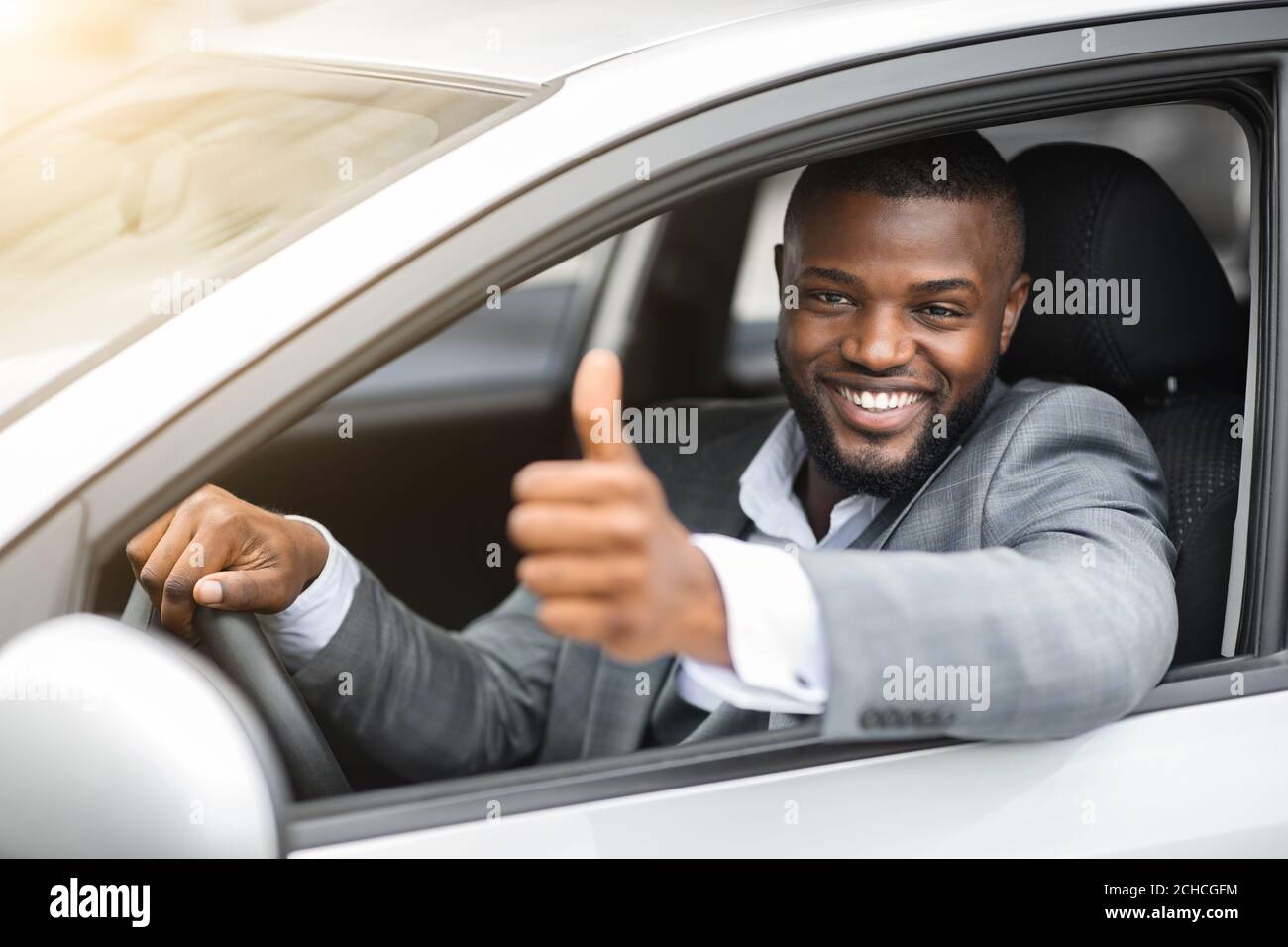 Joyeux homme d'affaires noir regardant à travers la fenêtre de voiture, montrant le pouce vers le haut Banque D'Images