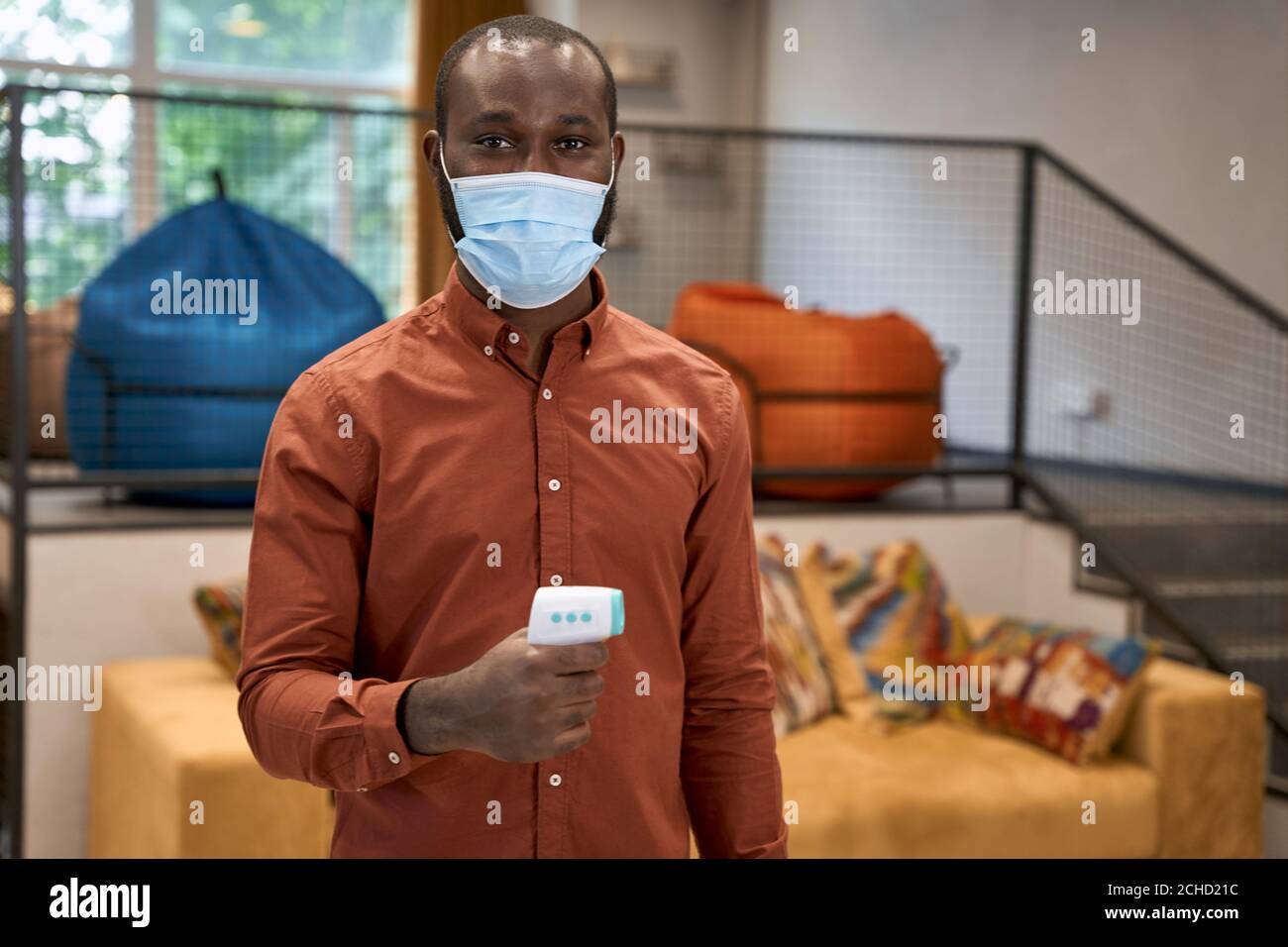 Portrait d'un jeune homme de bureau africain portant une protection médicale masque contenant le thermomètre infrarouge pour vérifier la température et regarder Banque D'Images
