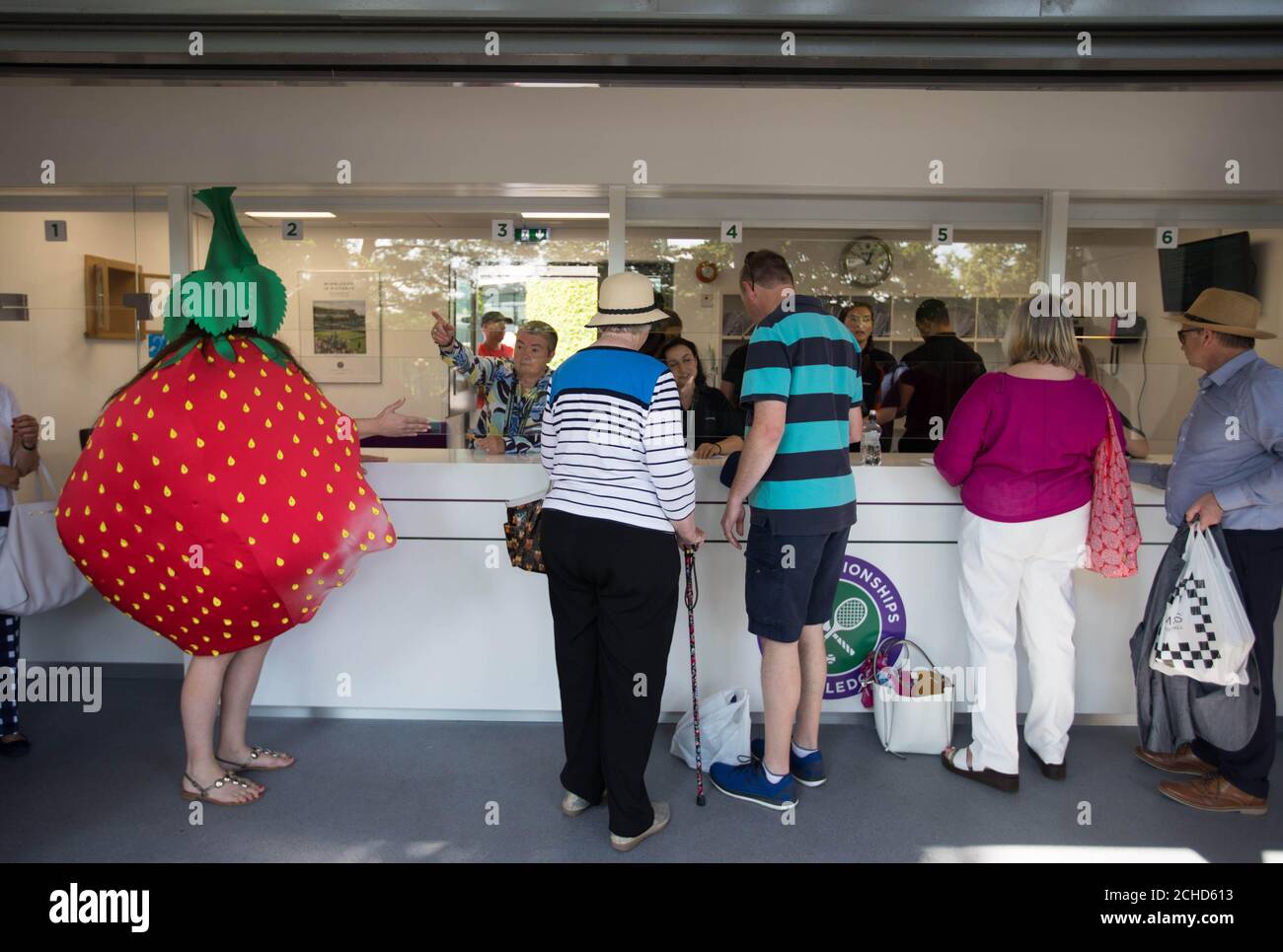 Un militant portant un costume de fraise wonky rejoint la file d'attente aux championnats de Wimbledon alors qu'Oddbox, le plus grand programme de boîte de fruits et légumes wonky du Royaume-Uni, fait prendre conscience du gaspillage au sein de l'industrie britannique des fraises, Londres. Banque D'Images