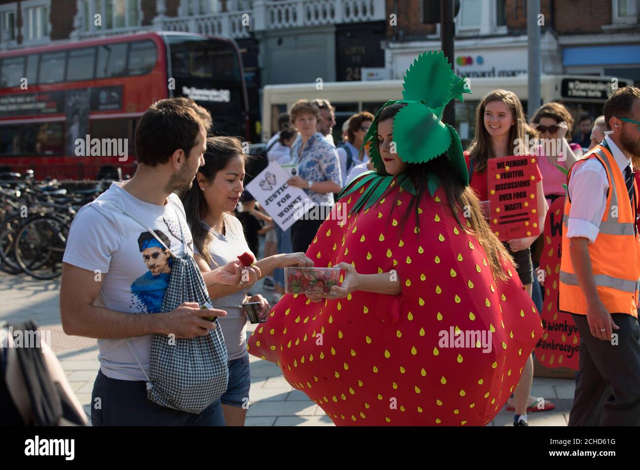 Un militant portant un costume de fraise wonky rejoint la file d'attente aux championnats de Wimbledon alors qu'Oddbox, le plus grand projet de boîte de fruits et légumes wonky du Royaume-Uni, fait prendre conscience du gaspillage au sein de l'industrie britannique des fraises, Londres. Banque D'Images