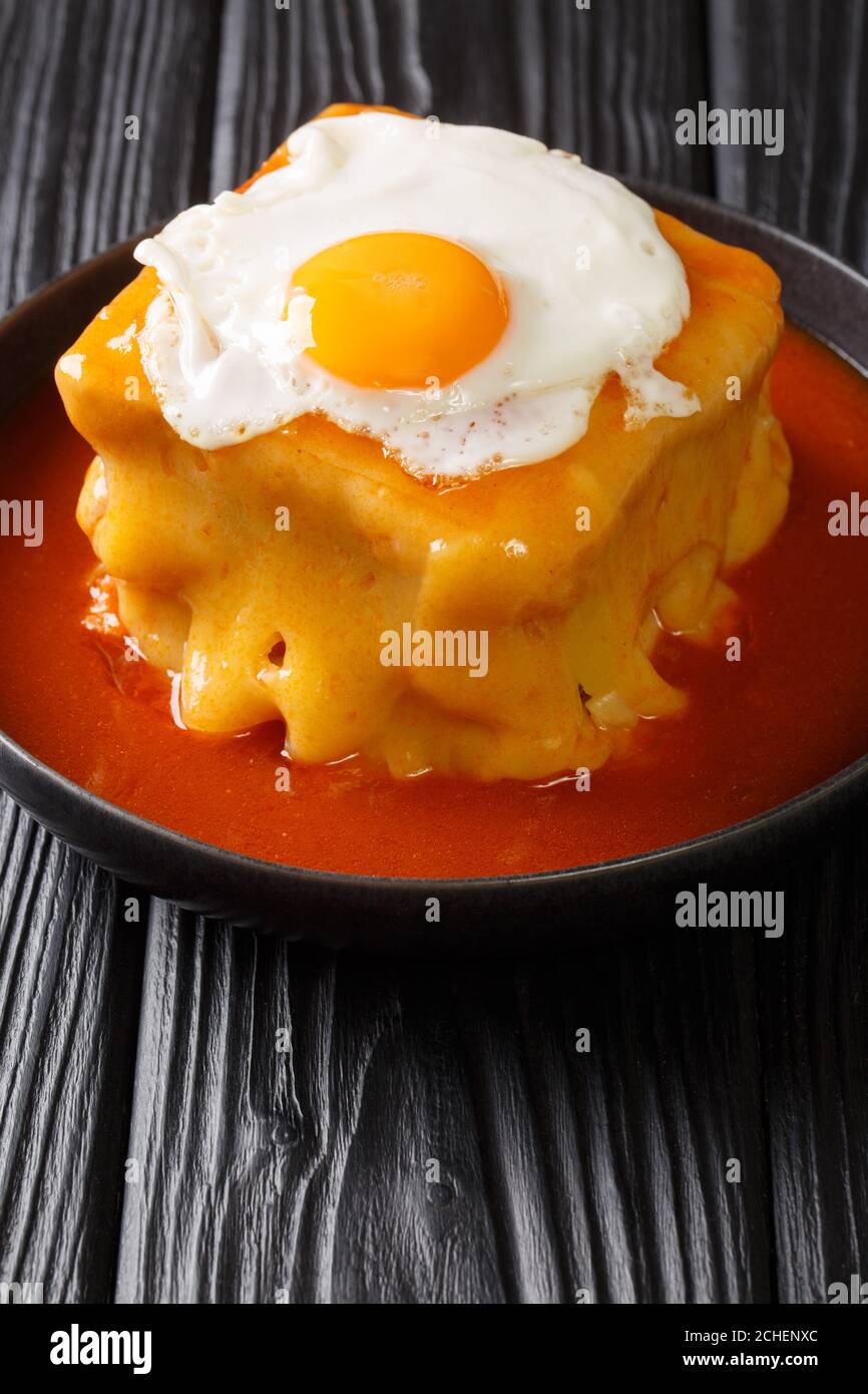 Sandwich Francesinha portugais chaud avec différents types de saucisses et de viande, versé avec une sauce à la bière de tomate et recouvert d'un œuf frit en gros plan Banque D'Images