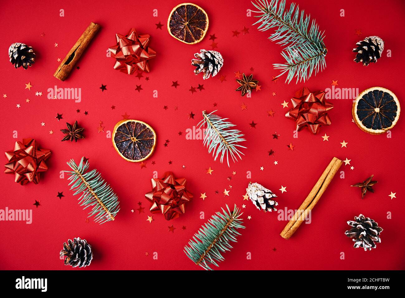 Composition de Noël. Branches de sapin, cônes de pin, fruits secs et confettis festifs sur fond rouge, vue du dessus Banque D'Images
