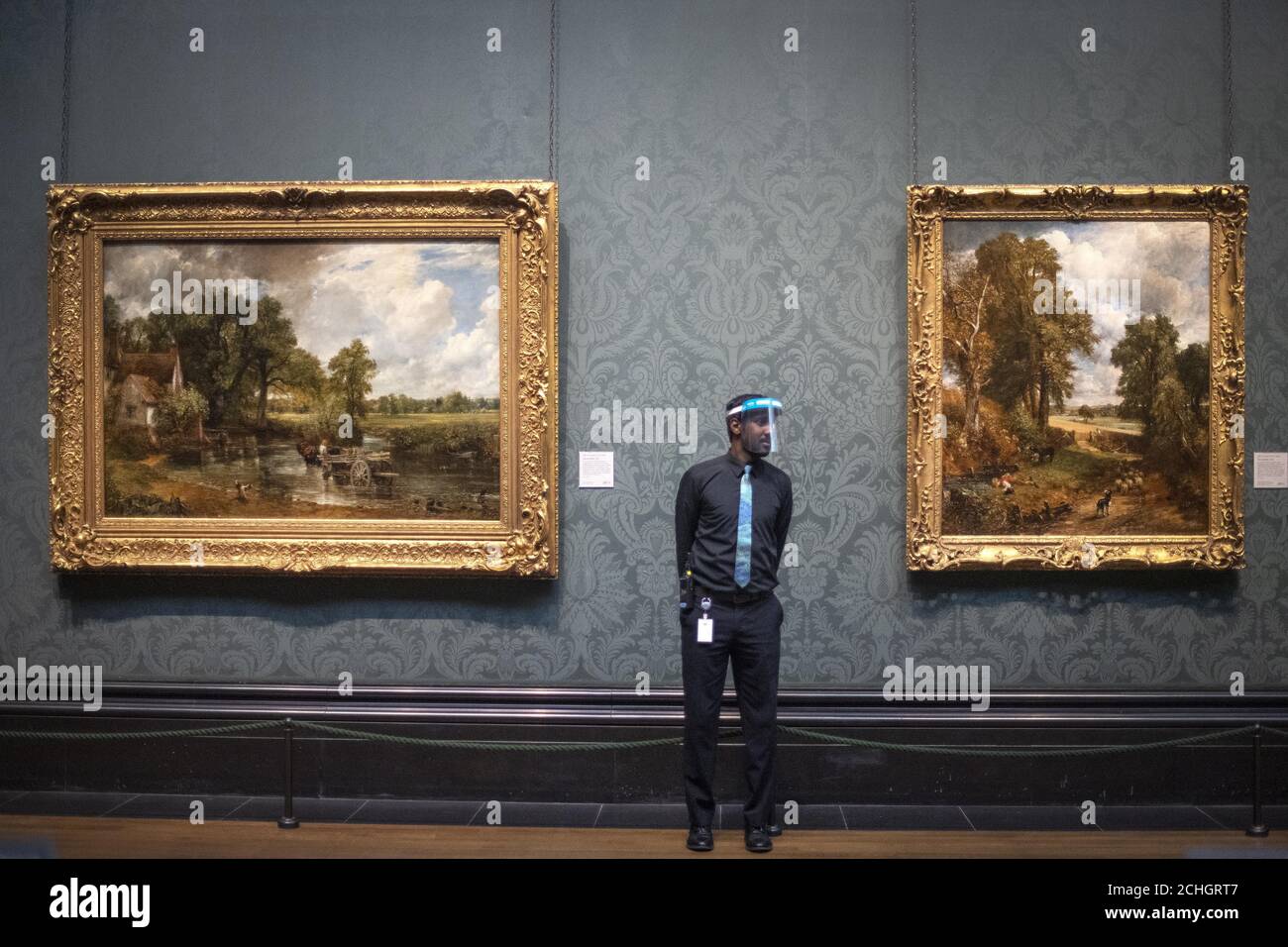 Un membre du personnel porte un pare-soleil tel qu'il est par le Hay Wain, 1821 ans, et le Cornfield, 1826 ans, par John Constable, Au National Portrait Gallery de Londres, alors qu'il se prépare à rouvrir après l'assouplissement des restrictions de confinement du coronavirus dans toute l'Angleterre. Banque D'Images
