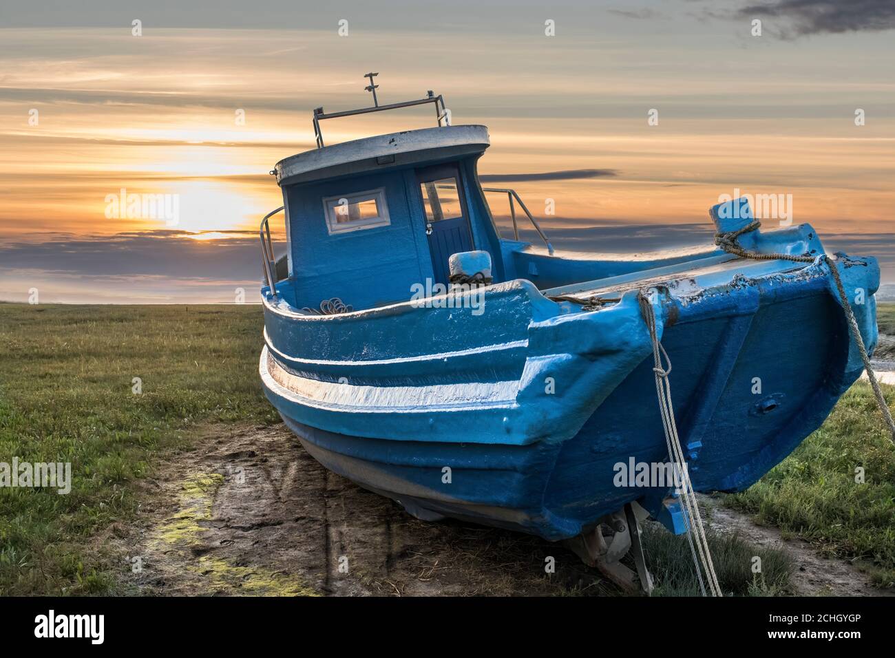 vieux bateau de pêche éclairé par le coucher du soleil à marée basse dedans estuaire Banque D'Images