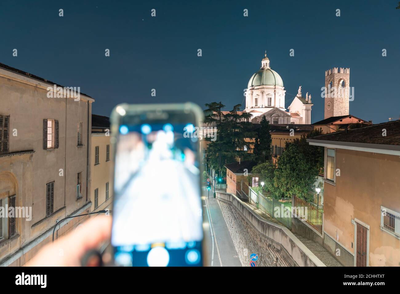 Vue de nuit avec smartphone, du dôme du Duomo Nuovo avec mouvement de la ville, église catholique romaine et tour du Palazzo del Broletto, HIS Banque D'Images