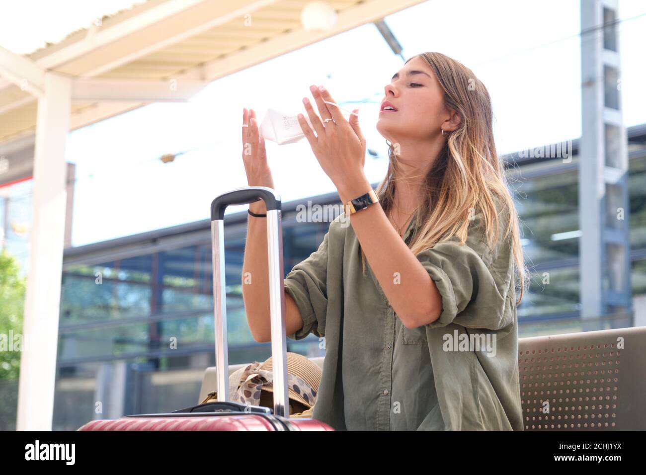 Jeune femme qui retire son masque à une gare. Concept de voyage et de coronavirus. Banque D'Images