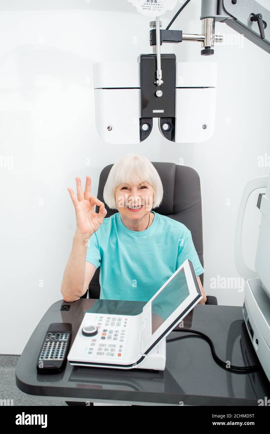Une femme âgée fait preuve d'un geste acceptable lorsqu'elle est assise dans le bureau d'un ophtalmologiste. Vérifier la vision de la femme avec le phoropter Banque D'Images