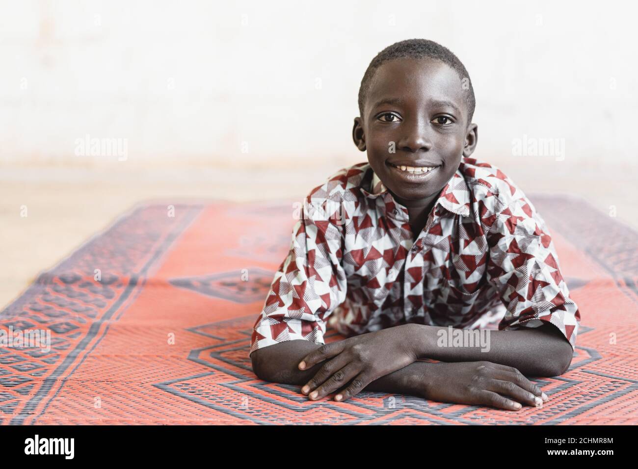 Mignon petit garçon africain avec un sourire en terre cuite sur une Afrique Tapis à motif Banque D'Images