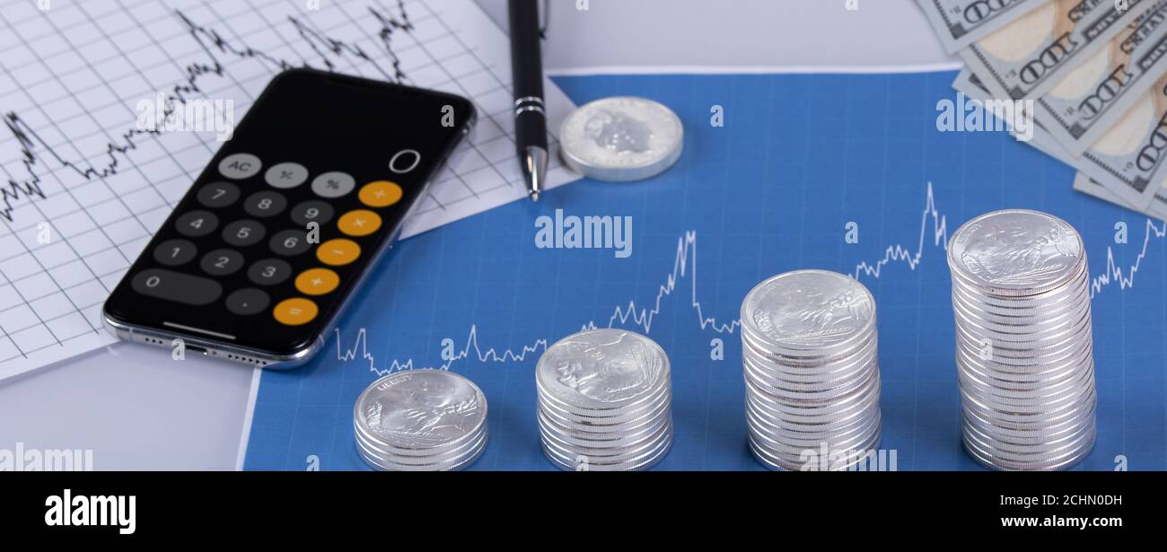 Piles de pièces d'argent avec tableaux de prix et calculatrice iPhone avec stylo. Concept investissement/comptabilité Banque D'Images