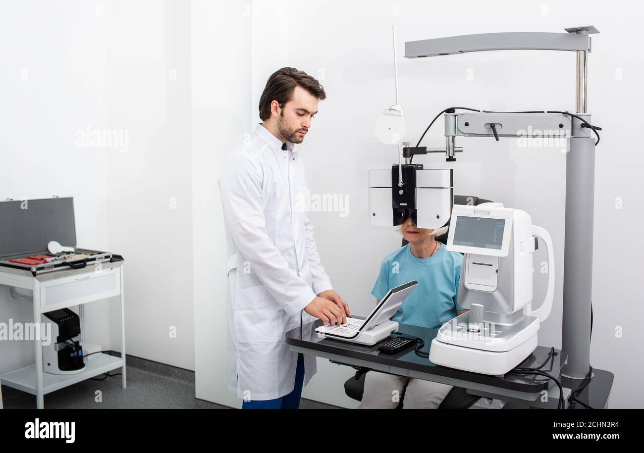 Optométriste sérieux expérimenté effectuant des tests sur site pour un patient utilisant un phoropter moderne dans une clinique médicale. Examen oculaire et diagnostic de la vision Banque D'Images