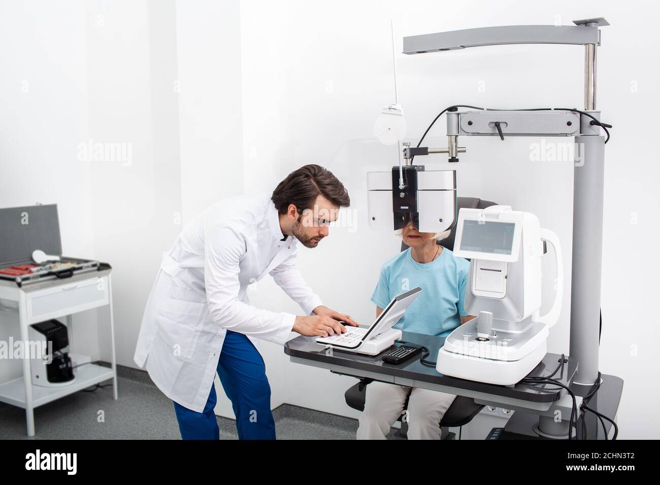 Optométriste sérieux expérimenté effectuant des tests sur site pour un patient utilisant un phoropter moderne dans une clinique médicale. Examen oculaire et diagnostic de la vision Banque D'Images