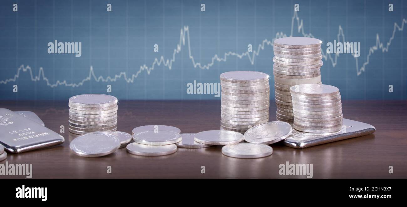 Barres et pièces en argent sur une table en bois avec tableau des prix en argent sur le mur. Concept d'investissement/marché Banque D'Images