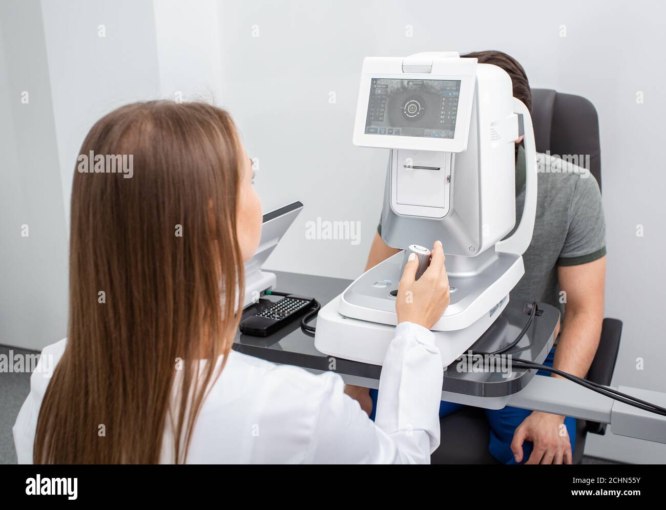 Femme médecin regardant très attentivement l'écran de l'auto-fractor ophtalmique pour vérifier correctement la vision de l'homme. Correction de la vision Banque D'Images