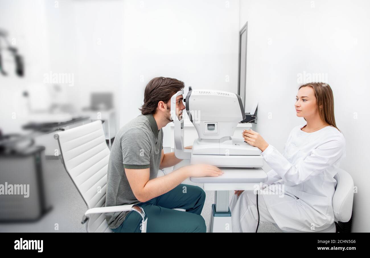 Une femme ophtalmologiste expérimentée utilisant un auto-fractor calcule la correction de la vision un patient d'homme dans un bureau ophtalmologique Banque D'Images