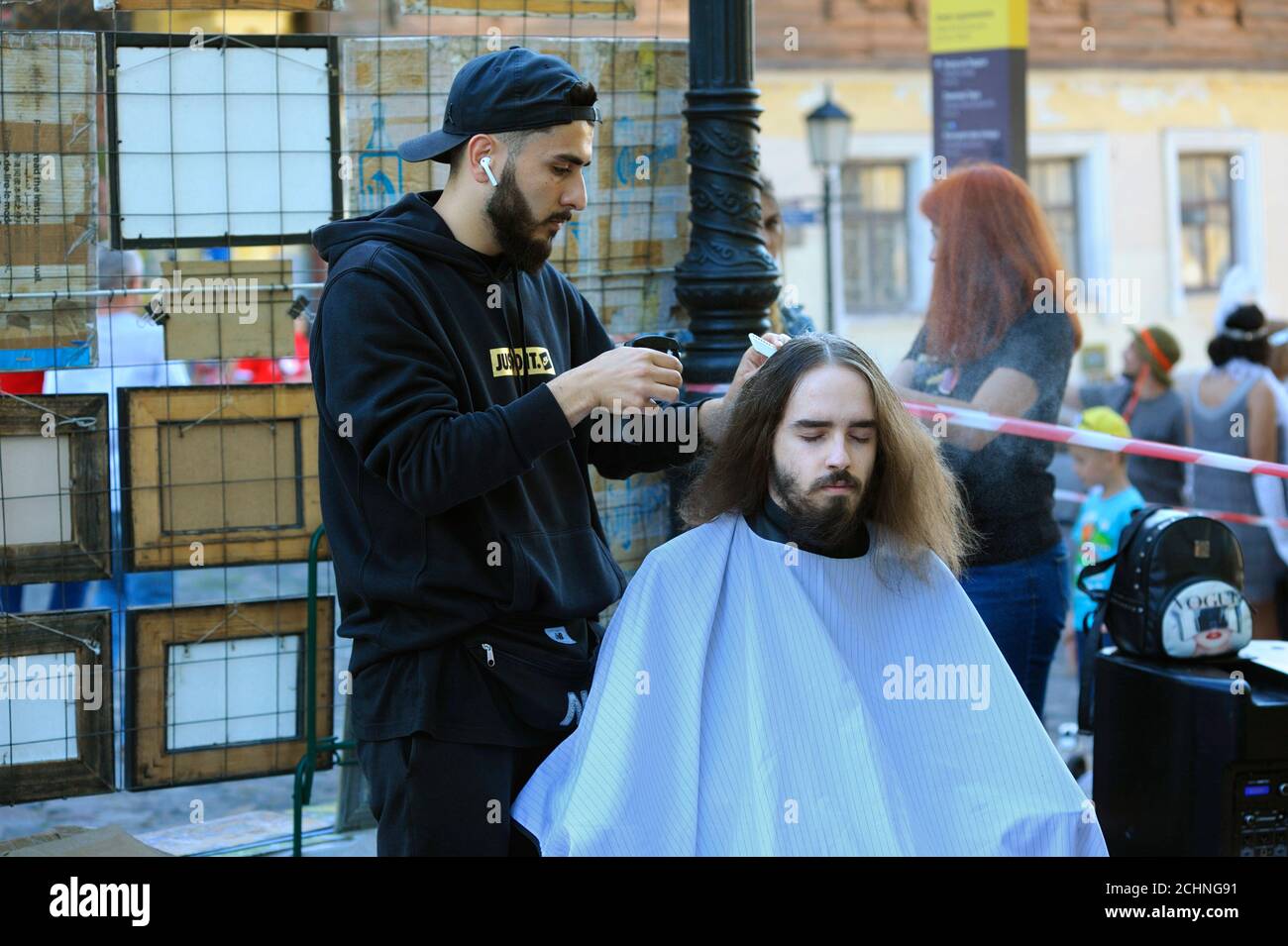 Street barber faisant les cheveux de jeune homme dans la rue, les gens marchant sur un fond Banque D'Images