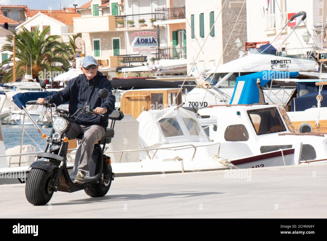 Vodice, Croatie - 1er septembre 2020 : homme senior à bord d'un scooter électrique à roue large avec siège, sur le quai d'une petite ville méditerranéenne Banque D'Images