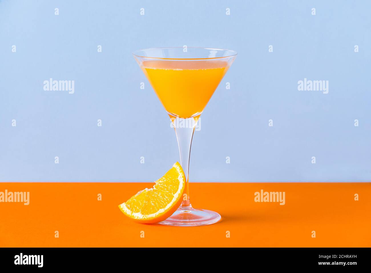 Jus d'orange frais dans un verre avec une tranche à la base sur une surface orange et un bleu clair arrière-plan Banque D'Images