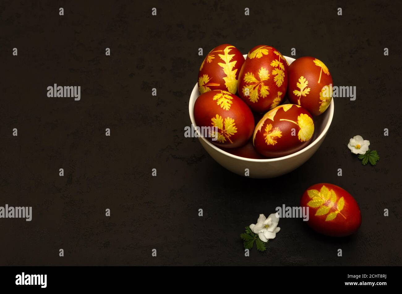 Oeufs de Pâques teints avec des pelures d'oignon avec un modèle de feuilles fraîches de plantes dans un bol blanc sur fond noir. BRICOLAGE. Maquette de carte de Pâques Banque D'Images