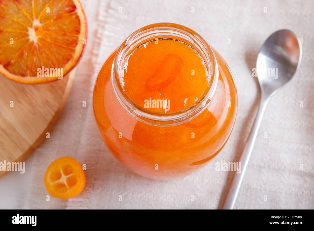 Confiture d'orange et de kumquat dans un pot en verre avec des fruits frais sur une nappe blanche. Maison, gros plan. Banque D'Images