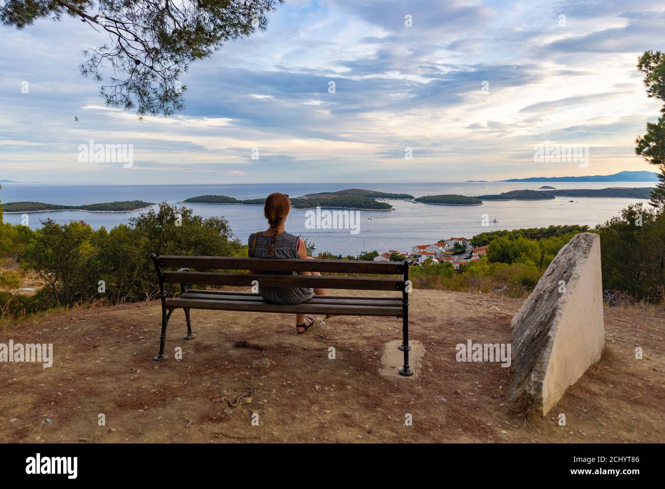 Belle fille assise seule sur le banc au point de vue de la colline de l'île de Hvar, regardant le magnifique coucher de soleil sur la mer Adriatique et les îles Paklinski dans le Th Banque D'Images Belle fille assise seule sur le banc au point de vue de la colline de l'île de Hvar, regardant le magnifique coucher de soleil sur la mer Adriatique et les îles Paklinski dans le Th Banque D'Images