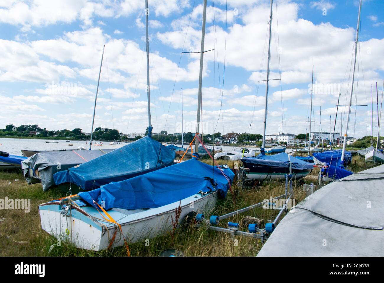 Petits bateaux de voile ou de pêche sur terre avec des mâts et des couvertures sur Mudeford Quay, dans le sud de l'Angleterre, beau ciel bleu ciel nuageux, beaucoup de dingies stockées sur Banque D'Images