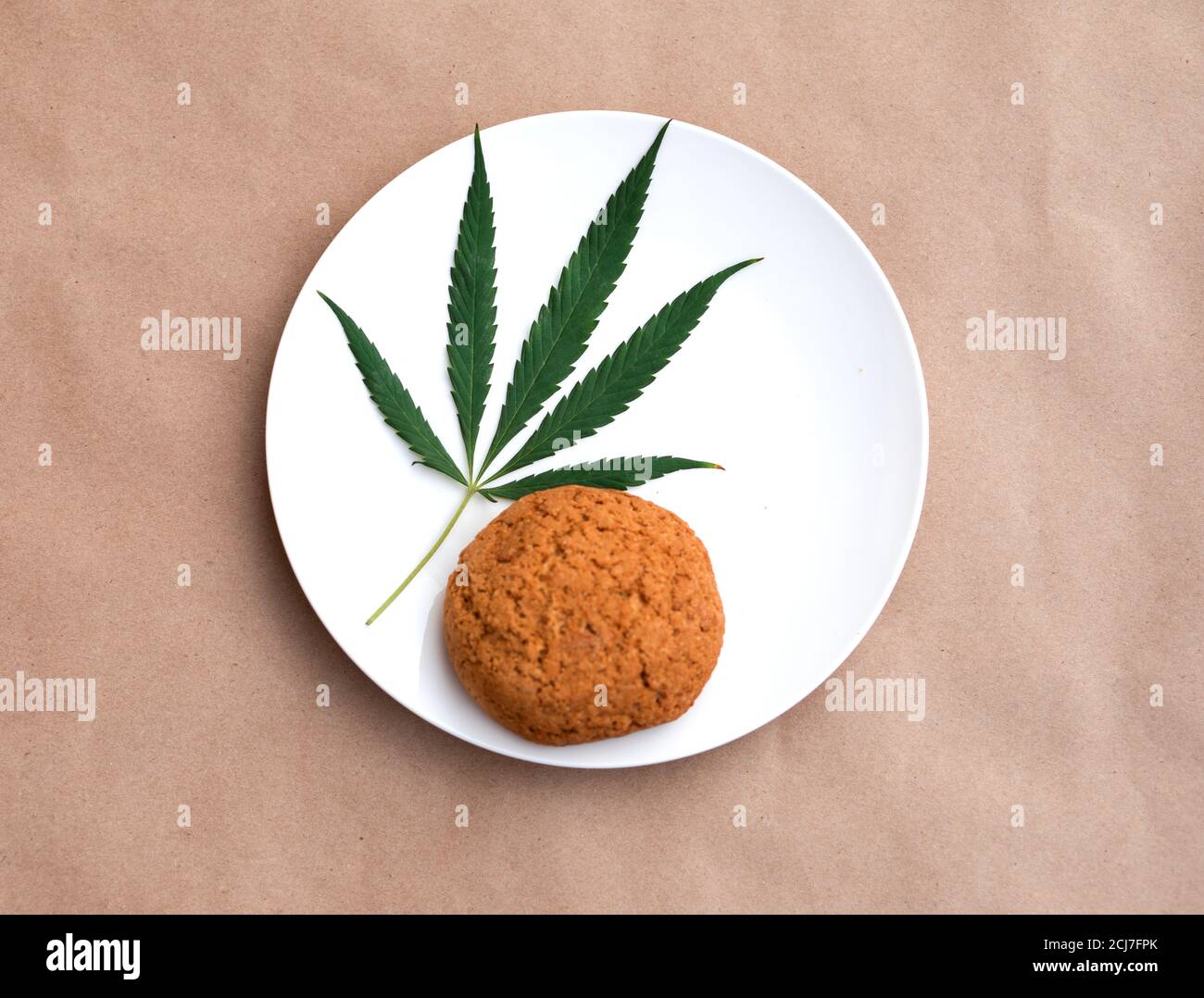 Feuille de cannabis avec biscuits sur une assiette blanche. Extraction de résine vivante de cannabis sur fond kraft. Banque D'Images