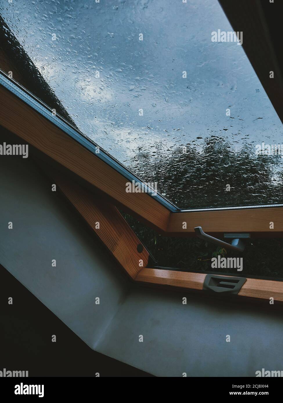 Fenêtre à moitié ouverte recouverte de gouttes de pluie pendant une journée nuageux Banque D'Images