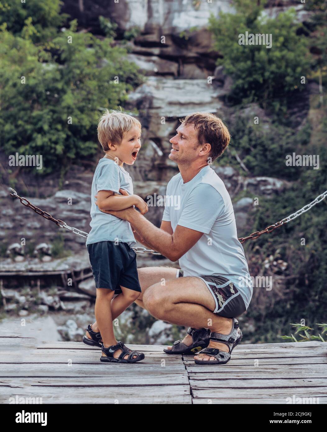 Le père s'enharle chatouiller son assis, sourire. Enfance heureuse, fête des pères, montagne, arrière-plan de chaîne comme symbole de lien fort entre papa et Banque D'Images