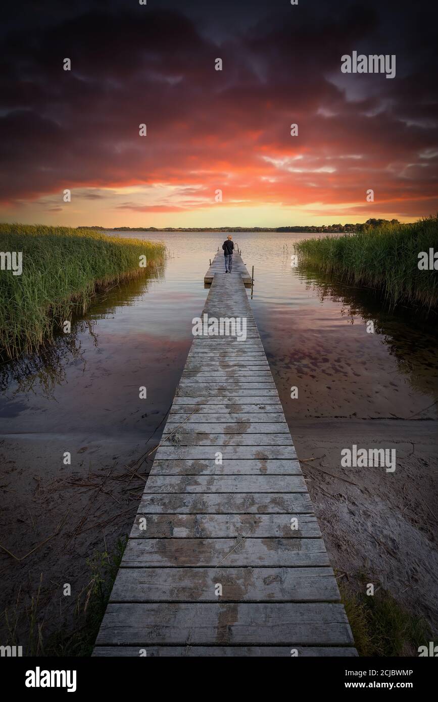 Une personne admire le coucher du soleil depuis une jetée en bois. Banque D'Images