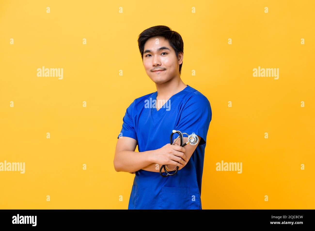 Jeune beau médecin asiatique homme souriant et faisant les bras croisés geste isolé sur fond jaune Banque D'Images