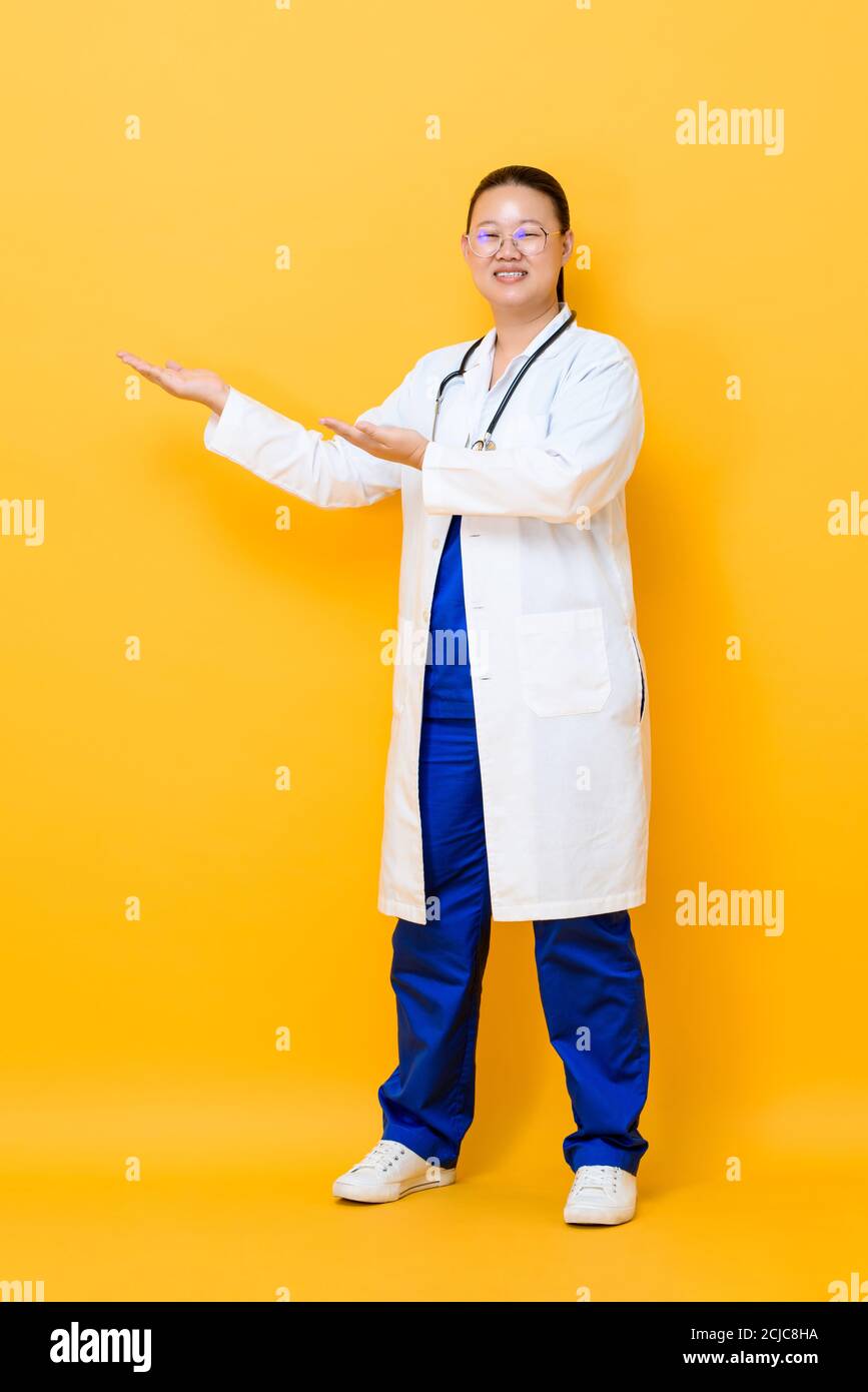 Jeune femme asiatique médecin debout et ouvrant les mains pour vider espace mis de côté isolé sur fond jaune Banque D'Images