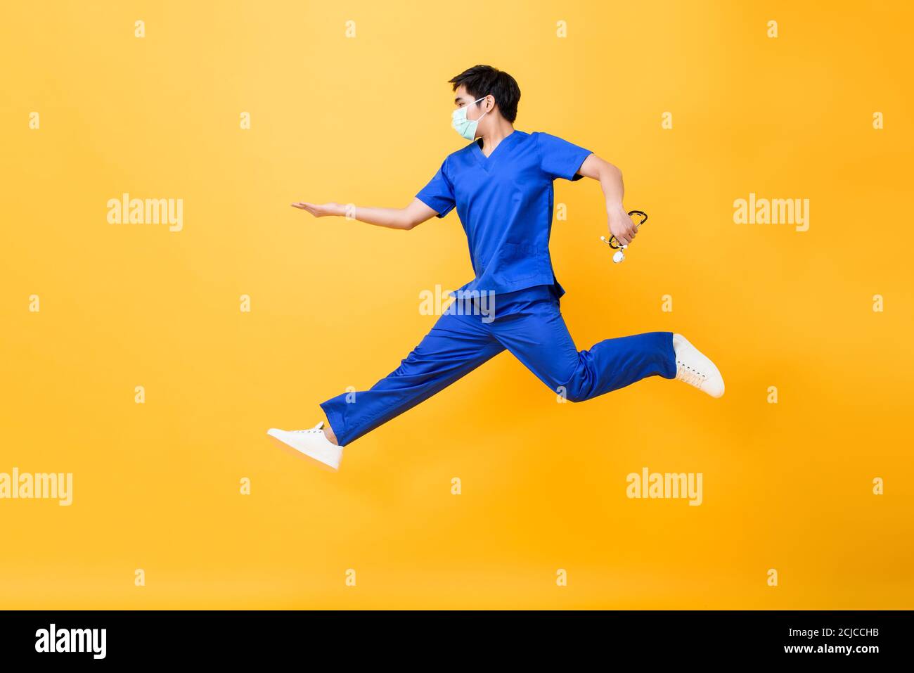 Portrait d'une jeune infirmière asiatique de sexe masculin tenant un stéthoscope sautant milieu de l'air sur fond jaune studio isolé Banque D'Images