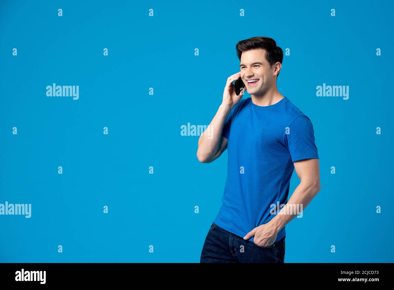 Portrait d'un jeune homme caucasien heureux ayant une conversation dessus téléphone portable dans un studio isolé sur fond bleu Banque D'Images