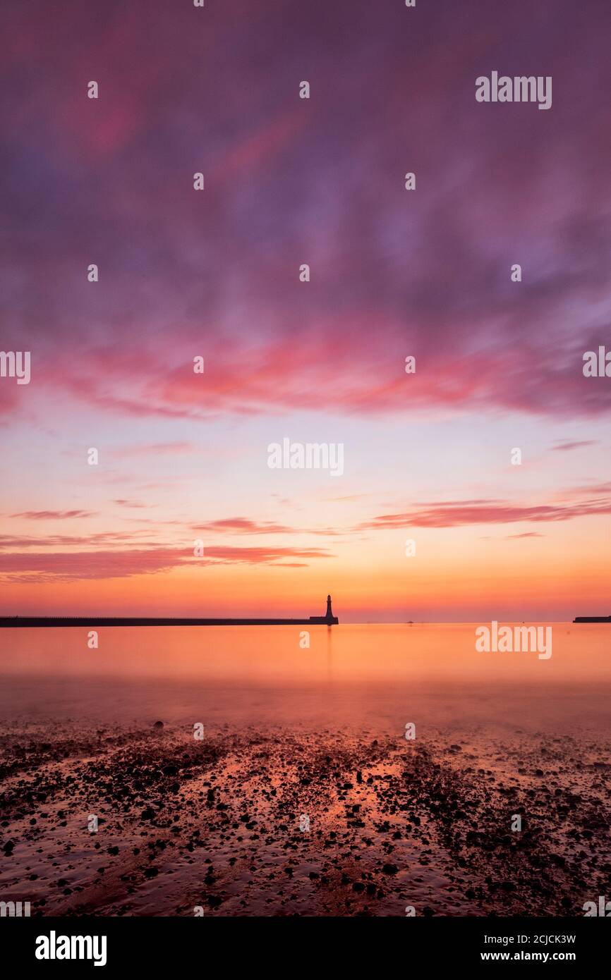 Le soleil se lève derrière le phare de Roker à Sunderland, dans le nord-est de l'Angleterre, peint le ciel orange et rose. Banque D'Images